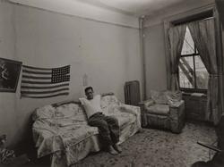 Untitled, [Man Sitting Alone in Room with Flag Draped on Wall], from East 100th Street series