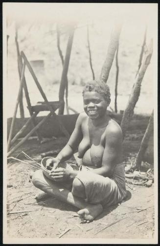 Smiling woman sitting down and weaving a basket