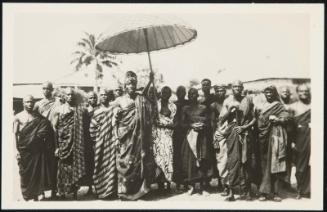 AFRICA - Native African tribal chief with staff of loyal followers. The huge umbrella protects his Majesty's royal head from the African sun.
