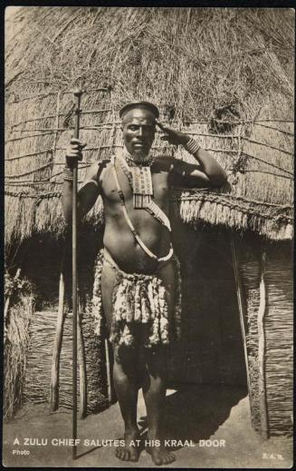 A ZULU CHIEF SALUTES AT HIS KRAAL DOOR