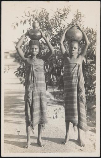 Two girls carrying water jugs above their heads