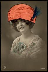 Smiling woman with red fabric hat, real hair and blue feathers.
