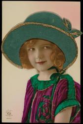Young girl in purple frock with green and gold fabric hat.
