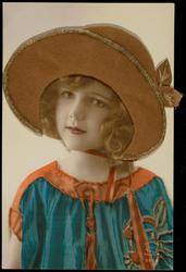 Young girl in blue frock with brown and gold fabric hat.
