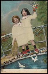 Two children in white with blue hats on a wooden bridge.
