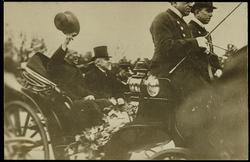 Woodrow Wilson waving his hat from a motor car.
