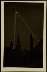 Zeppelin in the night sky with light beams from the ground.