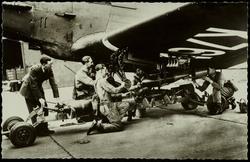 Un sous-officier de la Royal Air Force contrôle le chargement des bombes sur un appareil qui va partir en mission. 
Loading bombs into a R.A.F. machine prior to its taking off for a patrol flight.