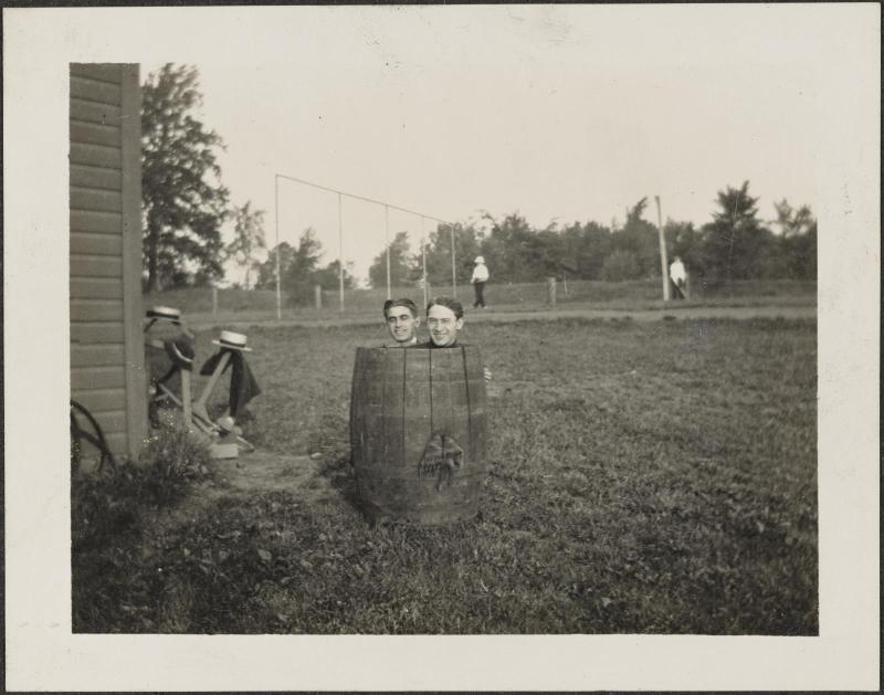 Two men, one in a barrel and one behind in field