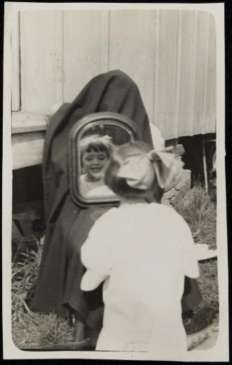 Girl with bow looking in mirror on a chair