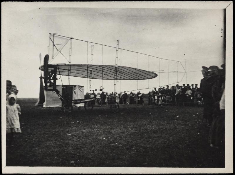 Airplane wing and frame on view in field with crowd of figures