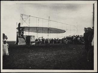 Airplane wing and frame on view in field with crowd of figures