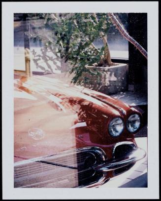 Close-up view through window of hood and headlight of a red Corvette 