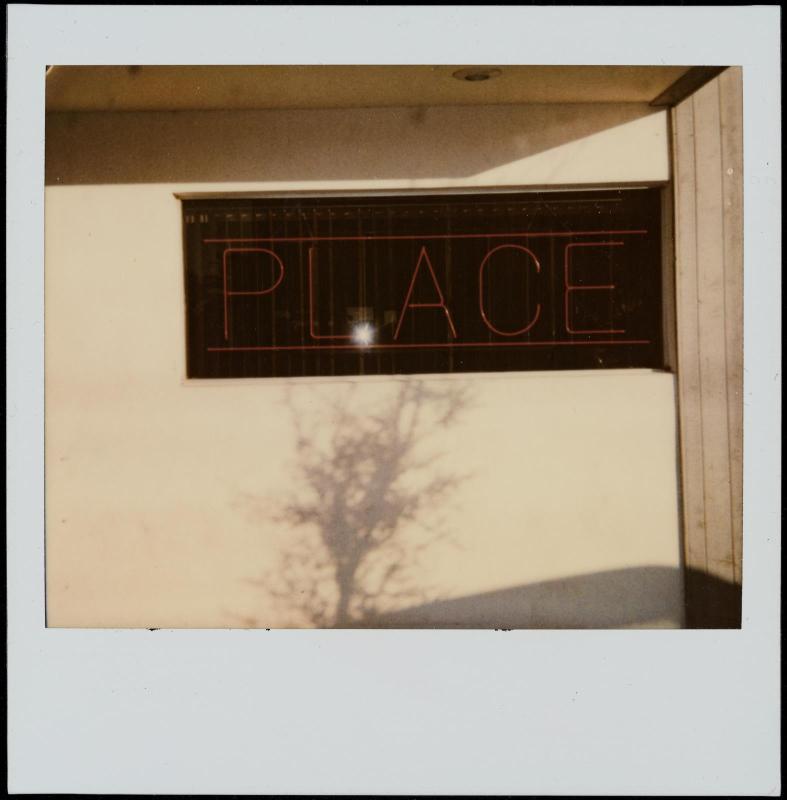 Red neon sign "PLACE" in window with shadow of tree