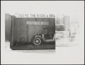 Automobile under "Give the Kids a Brake" sign