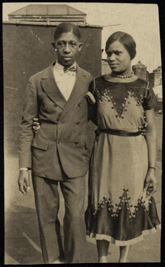 Young couple with arms around each other posed in front of backdrop outdoors