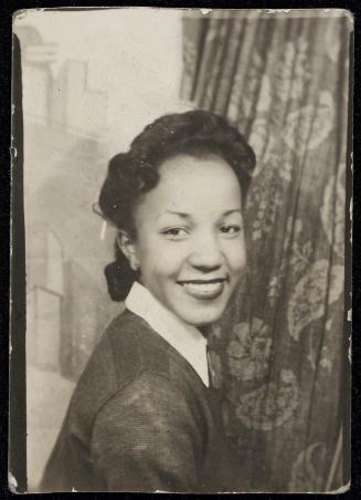 Portrait of young woman looking over her shoulder and set against painted background and patterned curtain