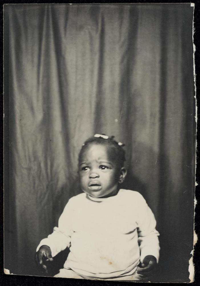 Portrait of a toddler seated in front of a curtain and looking as though about to cry