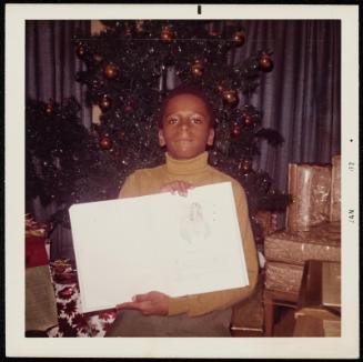 Portrait of a young boy holding up drawing with Christmas tree and gifts behind him