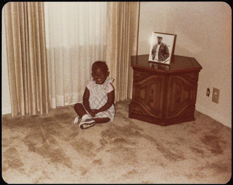 Small girl seated on the floor next to low table with framed portrait displayed on it