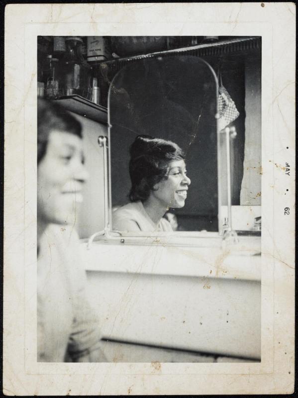 Double portrait of a woman seated in foreground and reflected in mirror