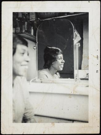 Double portrait of a woman seated in foreground and reflected in mirror