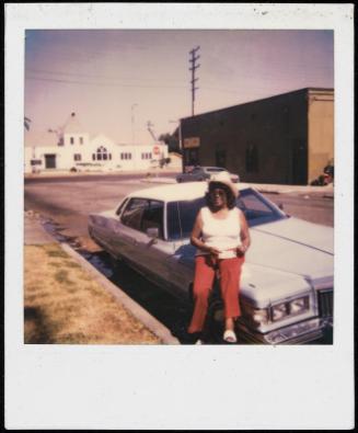 Portrait of a woman in red pants and cowboy hat seated on a car