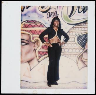 Portrait of young woman wearing cropped top and standing in front of painted mural with Egyptian motifs