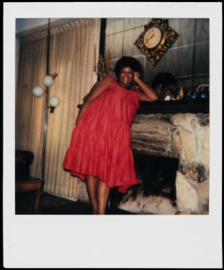 Portrait of a woman in a red dress leaning against a stone fireplace mantel