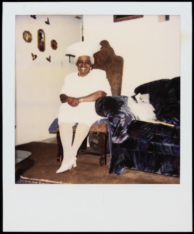Portrait of a woman seated in an interior, hands in lap, ankles crossed, and dressed all in white