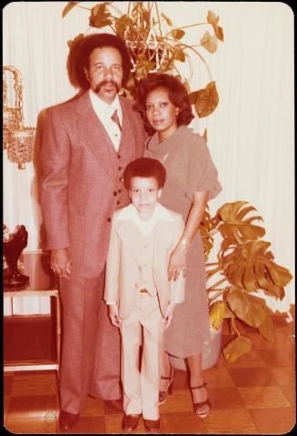 Family portrait of man, woman and young boy with large plant behind them
