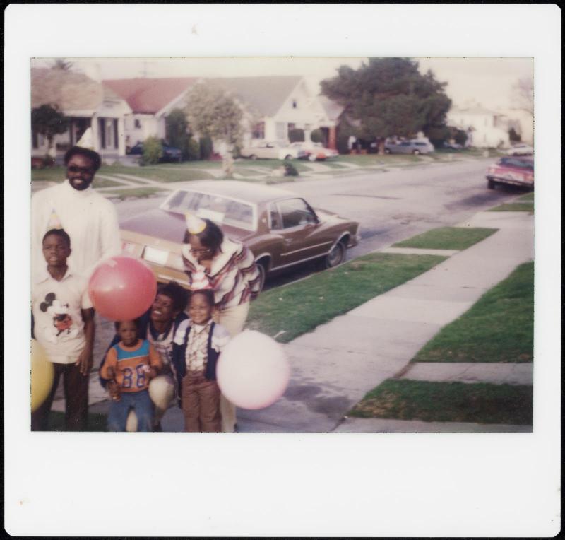 Family group with balloons on sidewalk with car behind them