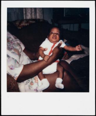 Baby dressed in red and white being held on woman's lap