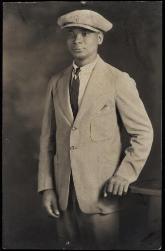 Studio portrait of a young man standing and wearing a soft cap and suit