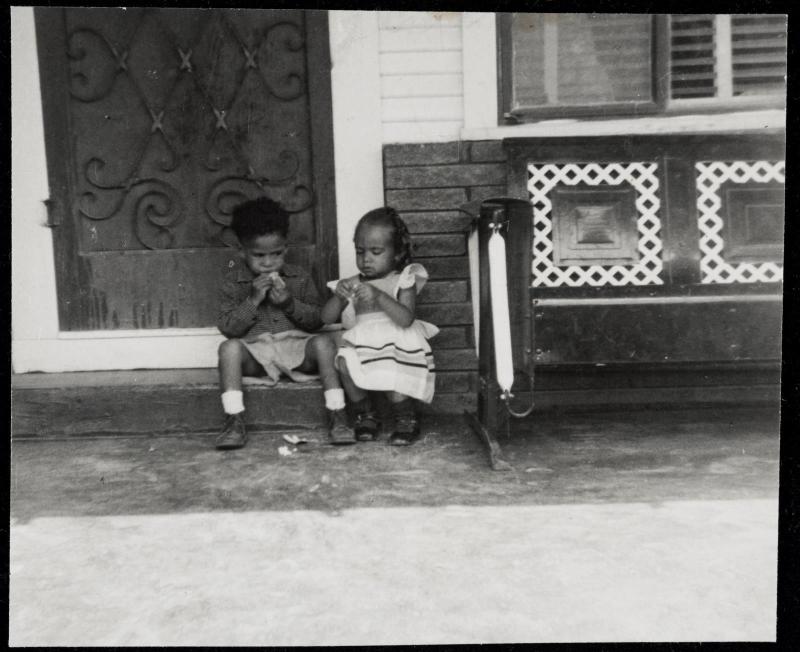 Two children seated together on a step next to a glider