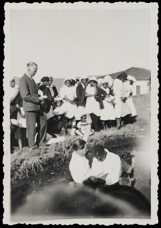 Scene of baptism with onlookers on shore