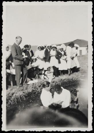 Scene of baptism with onlookers on shore