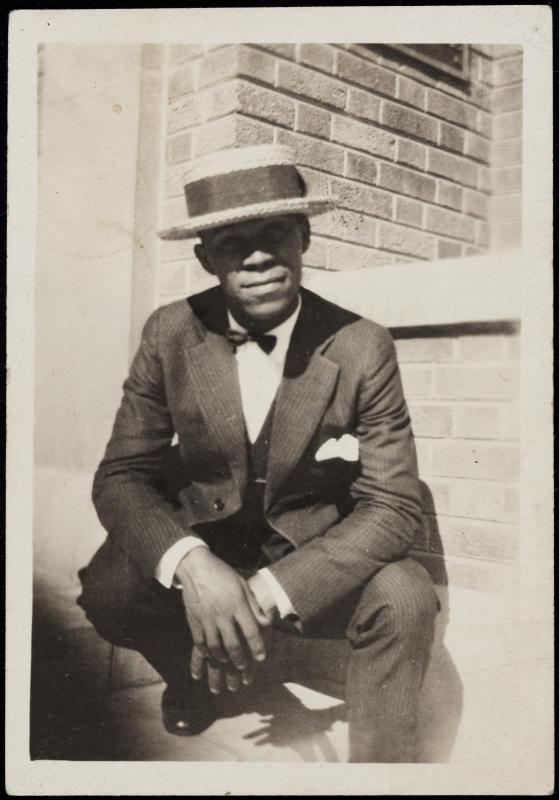 Crouching young man in boater hat, suit and bow tie