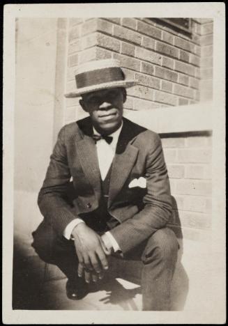 Crouching young man in boater hat, suit and bow tie