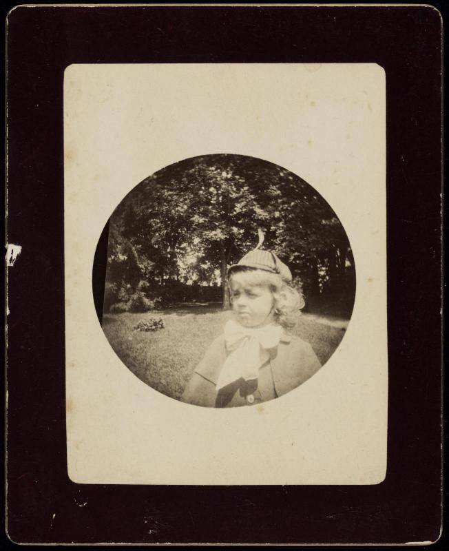 Young child outdoors wearing deerstalker hat and large bow tie at neck