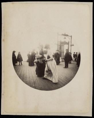 Two women walking in long skirts and hats on crowded pier or boardwalk