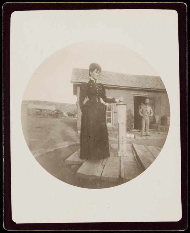 Woman standing next to decorative pillar in front of rustic building with man in doorway