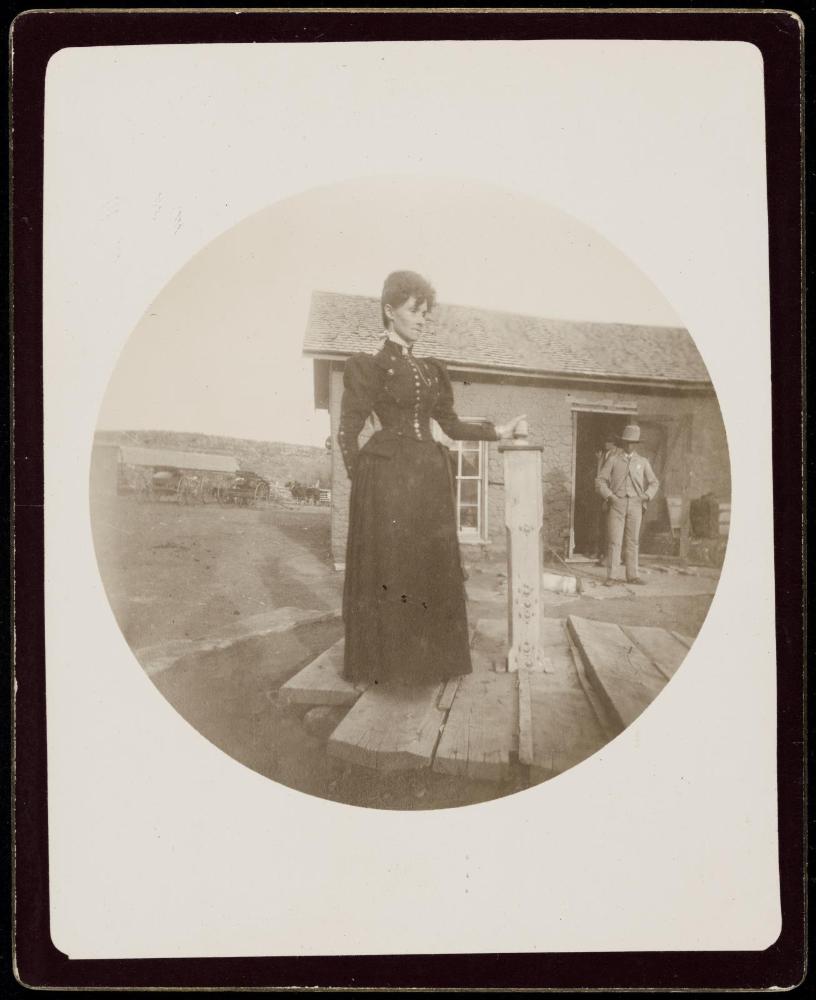 Woman standing next to decorative pillar in front of rustic building with man in doorway