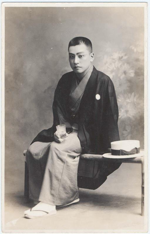 Seated man in hakama with drinking glass and boater hat