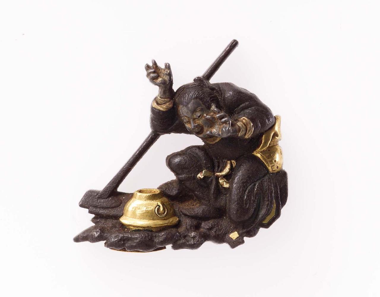 Menuki in the form of a seated figure surprised by a tea-kettle